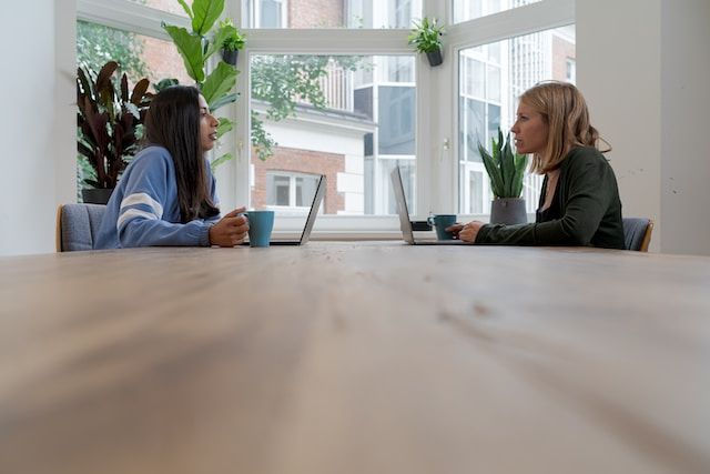 Two businesswomen sititing on a table facing each other and on their laptops
